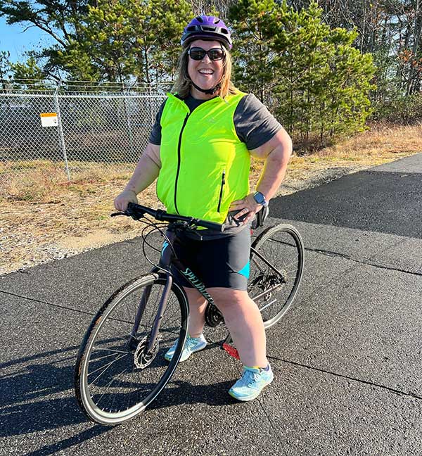 woman wearing bike helmet and safety vest standing with bike on paved trail
