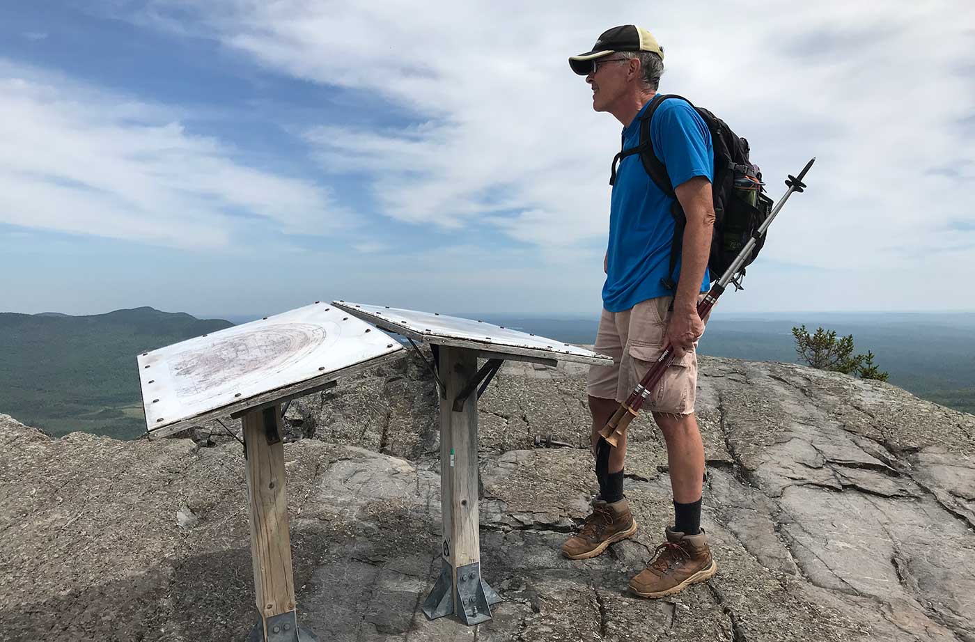 Man standing on mountaintop next to permanent map