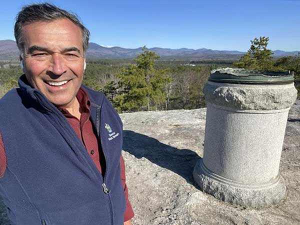 man smiling standing next to landmark on top of mountain