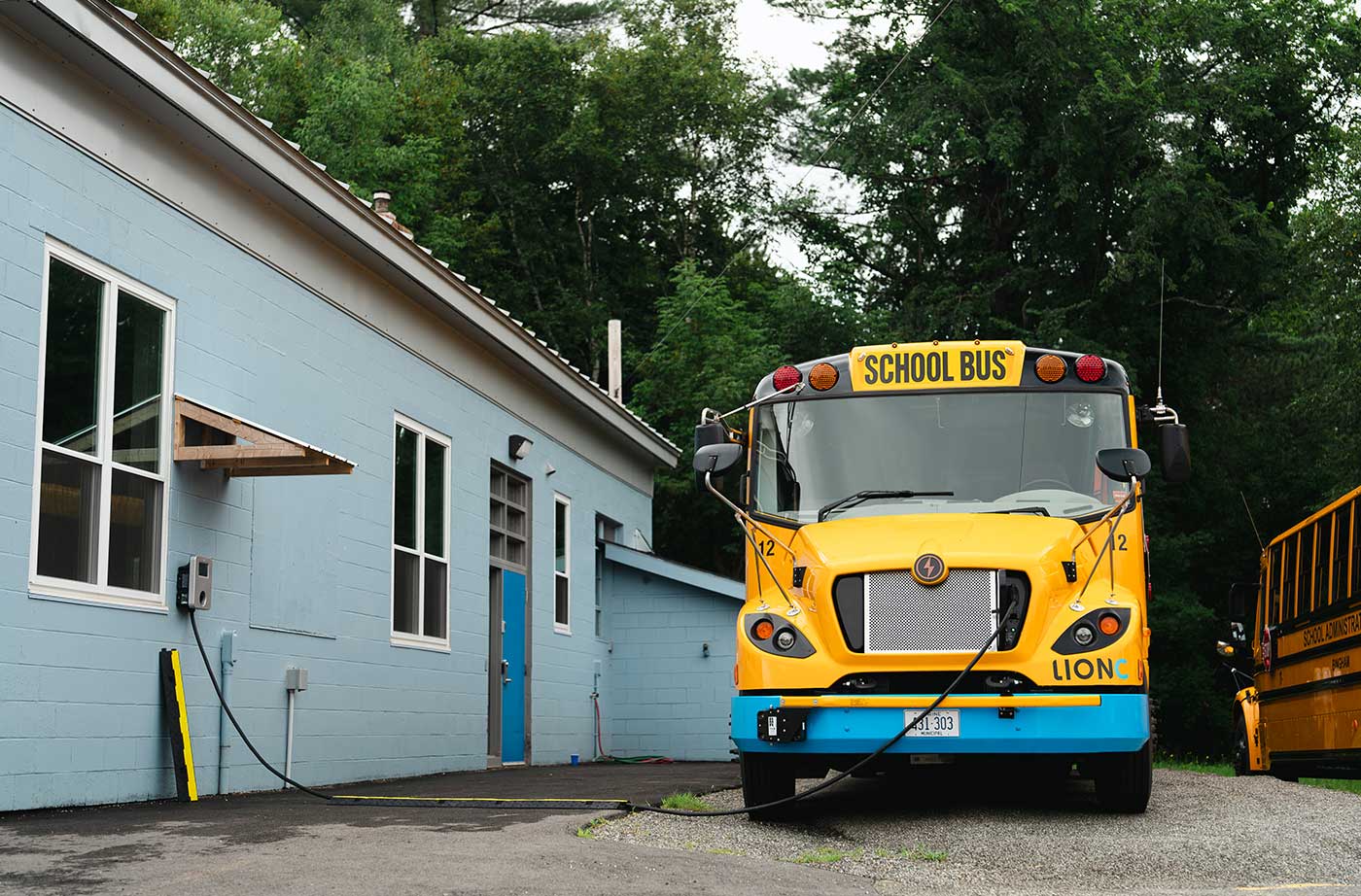 electric school bus parked outside school building, plugged into outlet for charging