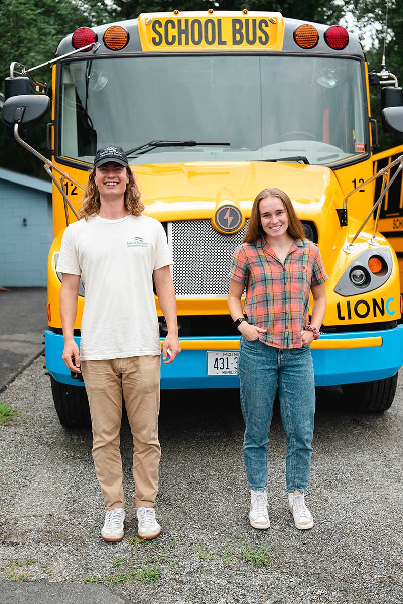 Two people smiling standing in front of electric bus