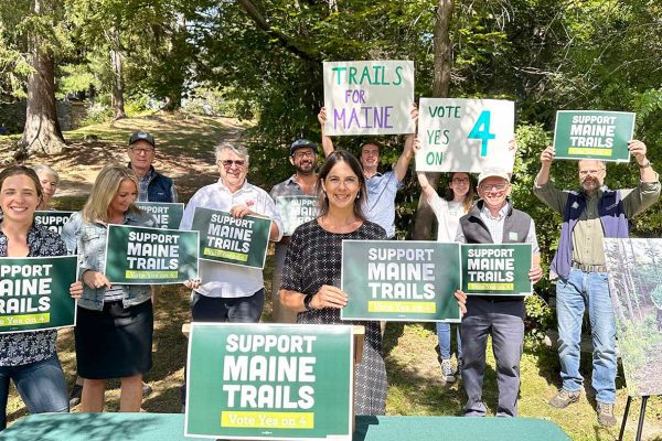 People smiling holding signs in support of Maine Trails Bond