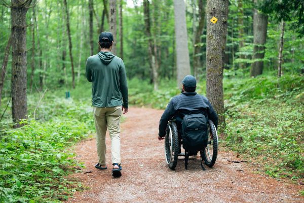 person walking and another person traveling on path in wheelchair