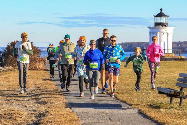 people running on trail with lighthouse behind them