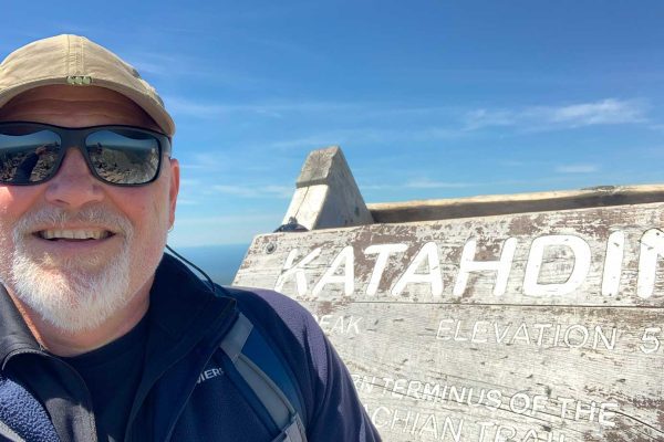 Todd smiling standing next to Katahdin sign at summit