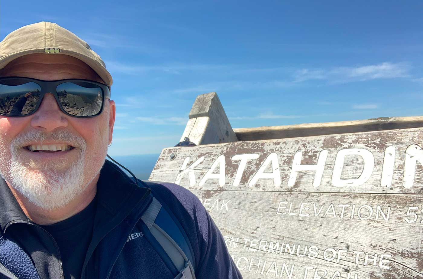 Todd smiling standing next to Katahdin sign at summit