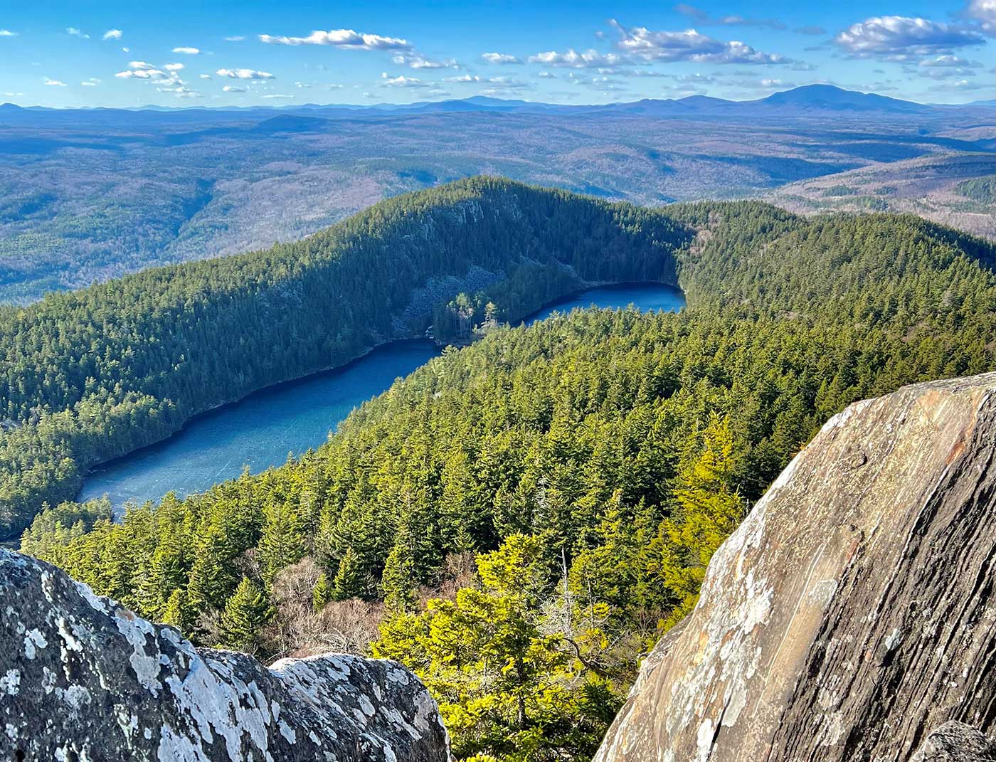 a view of mountains, forests, and some lakes in the forefront, with a blue sky full of wispy clouds