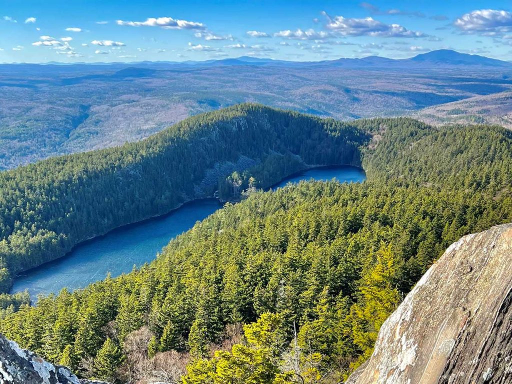 a view of mountains, forests, and some lakes in the forefront, with a blue sky full of wispy clouds