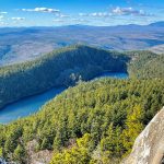 a view of mountains, forests, and some lakes in the forefront, with a blue sky full of wispy clouds