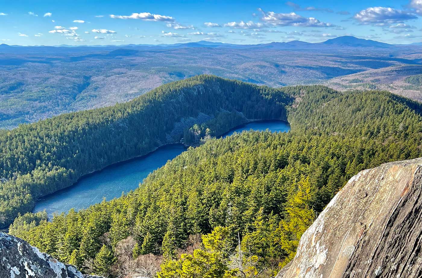 a view of mountains, forests, and some lakes in the forefront, with a blue sky full of wispy clouds