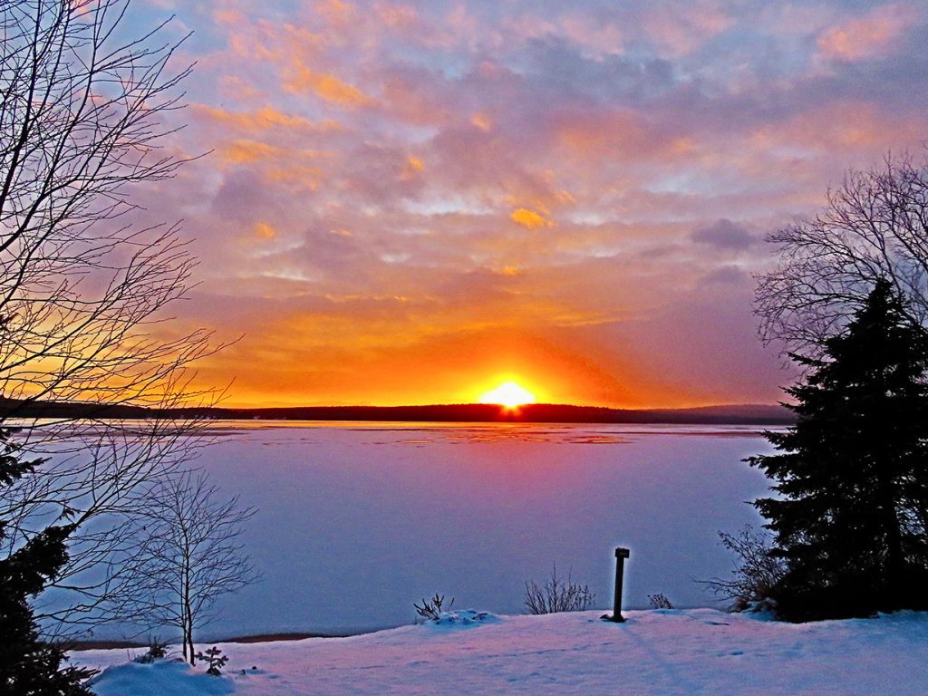 sunset with bright orange sun on horizon over lake and snow