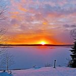 sunset with bright orange sun on horizon over lake and snow