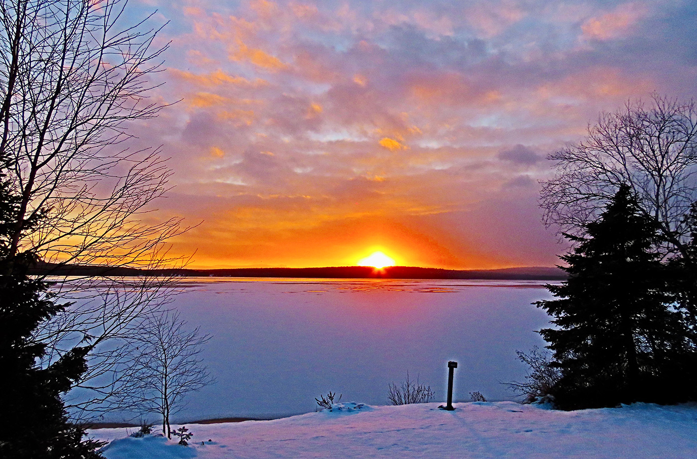 sunset with bright orange sun on horizon over lake and snow