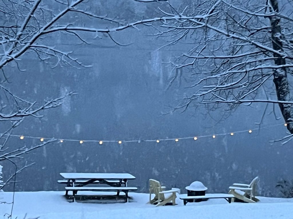 snowstorm over lake, with snow-covered picnic table, chairs, and firepit