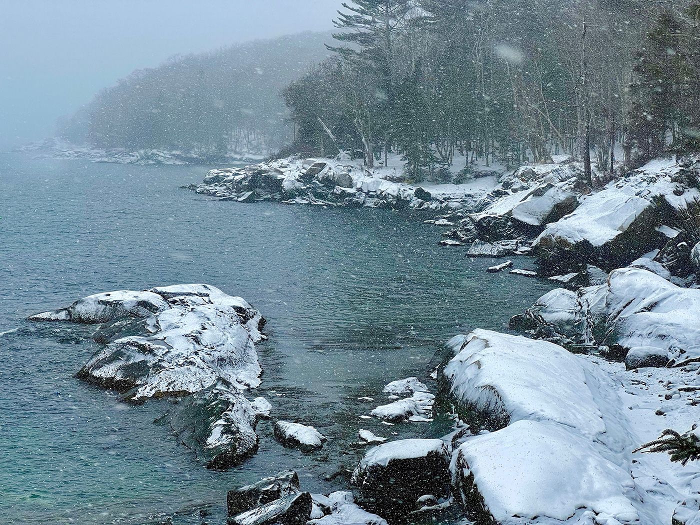 snow falling over river and snow-covered rocks