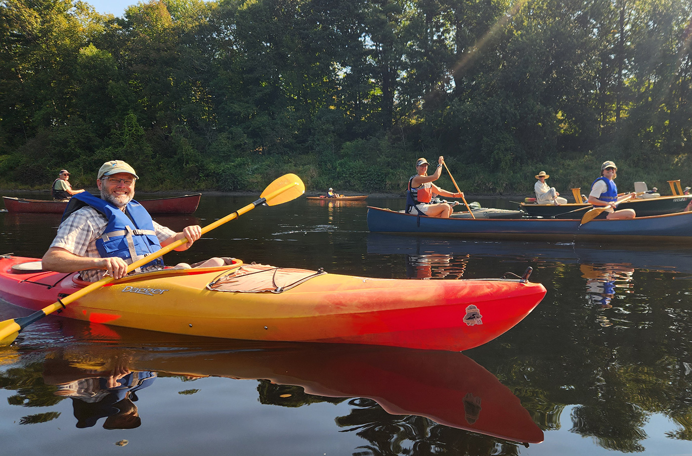 Person smiling while paddling yellow and orange kayak on river